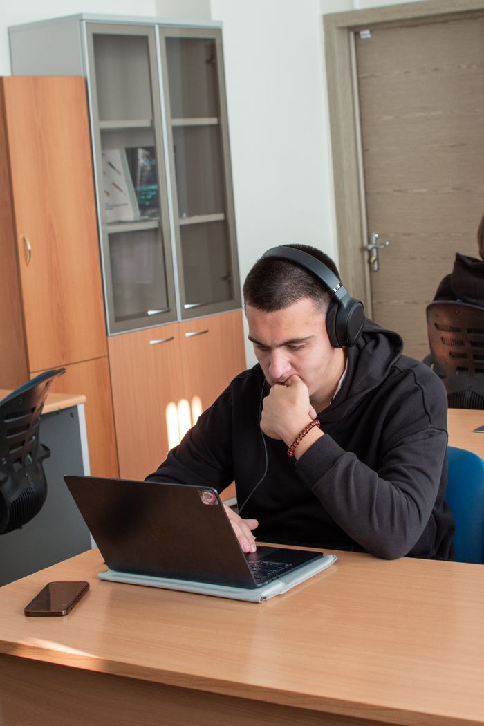 hero-gallery-01 A young man wearing headphones working intently on a laptop in a classroom.