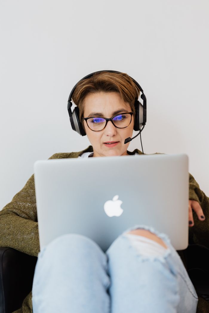 cta-01 Young woman focused on laptop screen, wearing a headset, working remotely indoors.