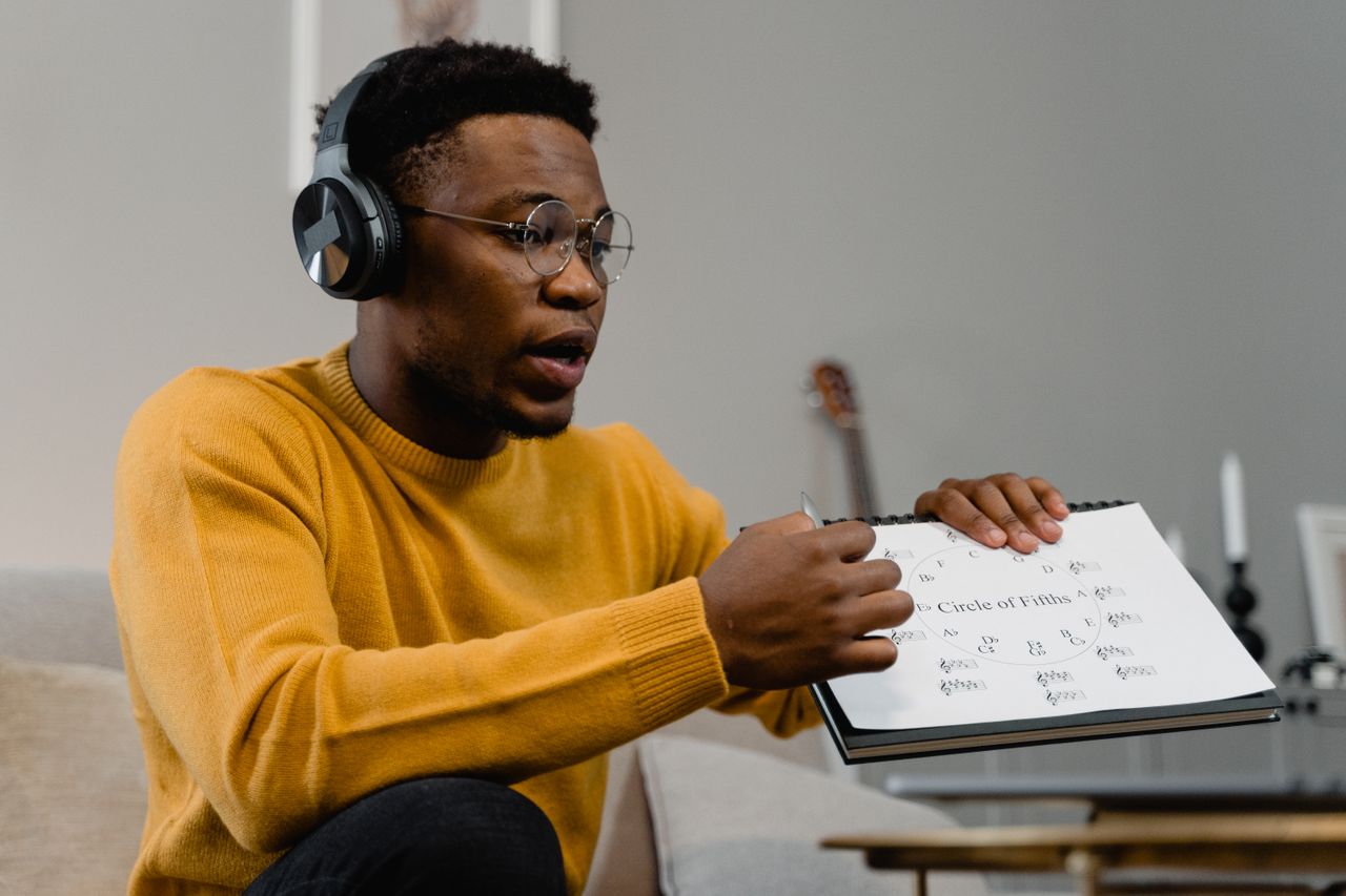 why-choose-us-img African American man wearing headphones, teaching music theory with sheet. Indoor setting.