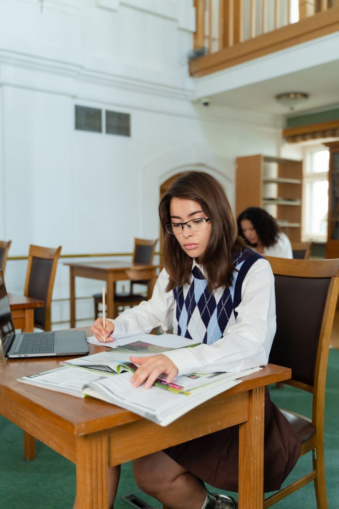 Young woman in a library, focused on studying with books and laptop.